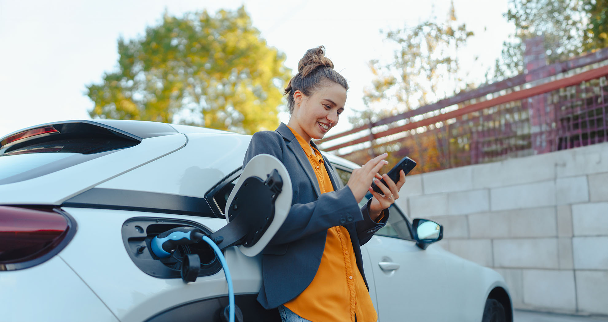 A woman standing by her car with her phone in her hand while her electric car charges