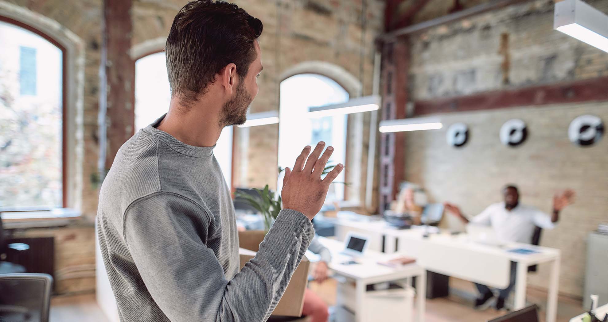A man waving to his colleague in an office.