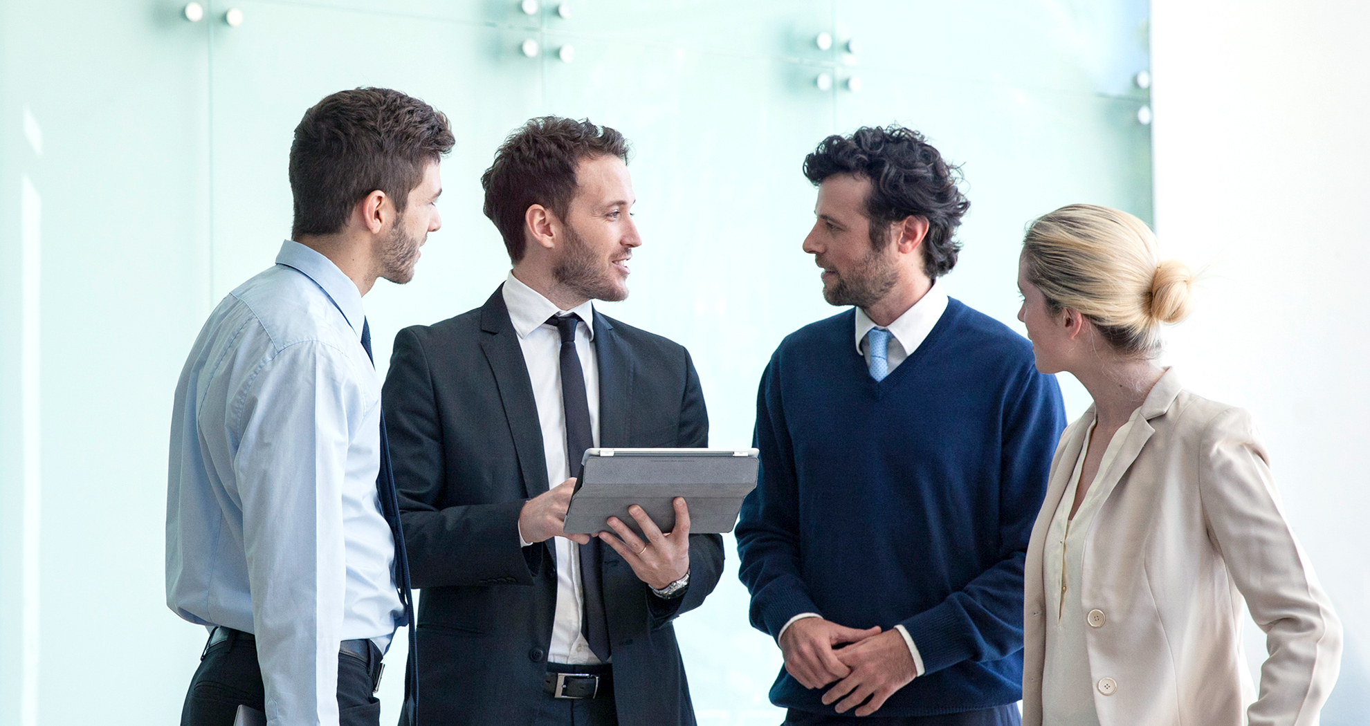 Four people in a boardroom standing up viewing a tablet screen